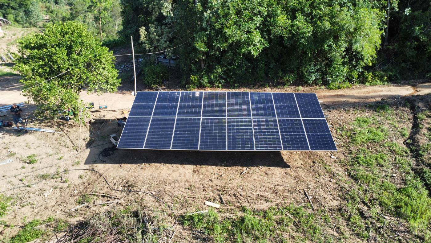 Vista aérea de sistema fotovoltaico em estrutura de solo, cercado por vegetação